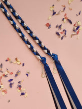 Load image into Gallery viewer, Intertwined Handfasting Cord made from silver, midnight blue and darkest blue coloured strands of satin ribbon, along with silver moon and star charms. Set against a pink backdrop with confetti.