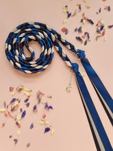 Load image into Gallery viewer, Intertwined Handfasting Cord made from silver, midnight blue and darkest blue coloured strands of satin ribbon, along with silver moon and star charms. Set against a pink backdrop with confetti.