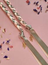 Load image into Gallery viewer, Intertwined Handfasting Cord made from cream, sage and peach coloured strands of satin ribbon, along with gold leaf charms. Set against a pink backdrop with confetti.