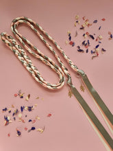 Load image into Gallery viewer, Intertwined Handfasting Cord made from cream, sage and peach coloured strands of satin ribbon, along with gold leaf charms. Set against a pink backdrop with confetti.