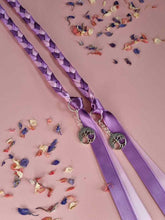 Load image into Gallery viewer, Intertwined Handfasting Cord made from mauve, lilac and lavender strands of satin ribbon, along with silver tree of life charms. Set against a pink backdrop with confetti.