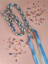 Load image into Gallery viewer, Intertwined Handfasting Cords made from blue, ivory and green strands of satin ribbon, along with silver anchor charms. Set against a pink backdrop with confetti.