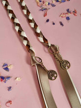 Load image into Gallery viewer, Intertwined Handfasting Cord made from green, cream and brown strands of satin ribbon along with gold tree of life charms. Set against a pink backdrop with confetti.