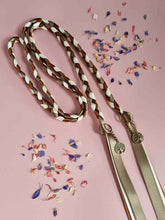 Load image into Gallery viewer, Intertwined Handfasting Cord made from green, cream and brown strands of satin ribbon along with gold tree of life charms. Set against a pink backdrop with confetti.