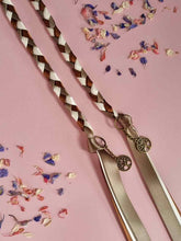 Load image into Gallery viewer, Intertwined Handfasting Cord made from green, cream and brown strands of satin ribbon along with gold tree of life charms. Set against a pink backdrop with confetti.