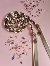 Load image into Gallery viewer, Intertwined Handfasting Cord made from green, cream and brown strands of satin ribbon along with gold tree of life charms. Set against a pink backdrop with confetti.