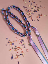 Load image into Gallery viewer, Intertwined Handfasting Cords made from mauve, blue and green strands of satin ribbon, along with silver celtic knot charms.  Set against a pink background with confetti.
