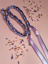 Load image into Gallery viewer, Intertwined Handfasting Cords made from mauve, blue and green strands of satin ribbon, along with silver celtic knot charms. Set against a pink background with confetti.