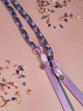 Load image into Gallery viewer, Intertwined Handfasting Cords made from mauve, blue and green strands of satin ribbon, along with silver celtic knot charms. Set against a pink background with confetti.