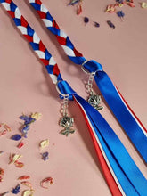 Load image into Gallery viewer, Intertwined Handfasting Cord made from red, white and blue strands of satin ribbon, along with silver rose charms. Set against a pink backdrop with confetti.