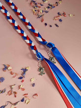 Load image into Gallery viewer, Intertwined Handfasting Cord made from red, white and blue strands of satin ribbon, along with silver rose charms. Set against a pink backdrop with confetti.