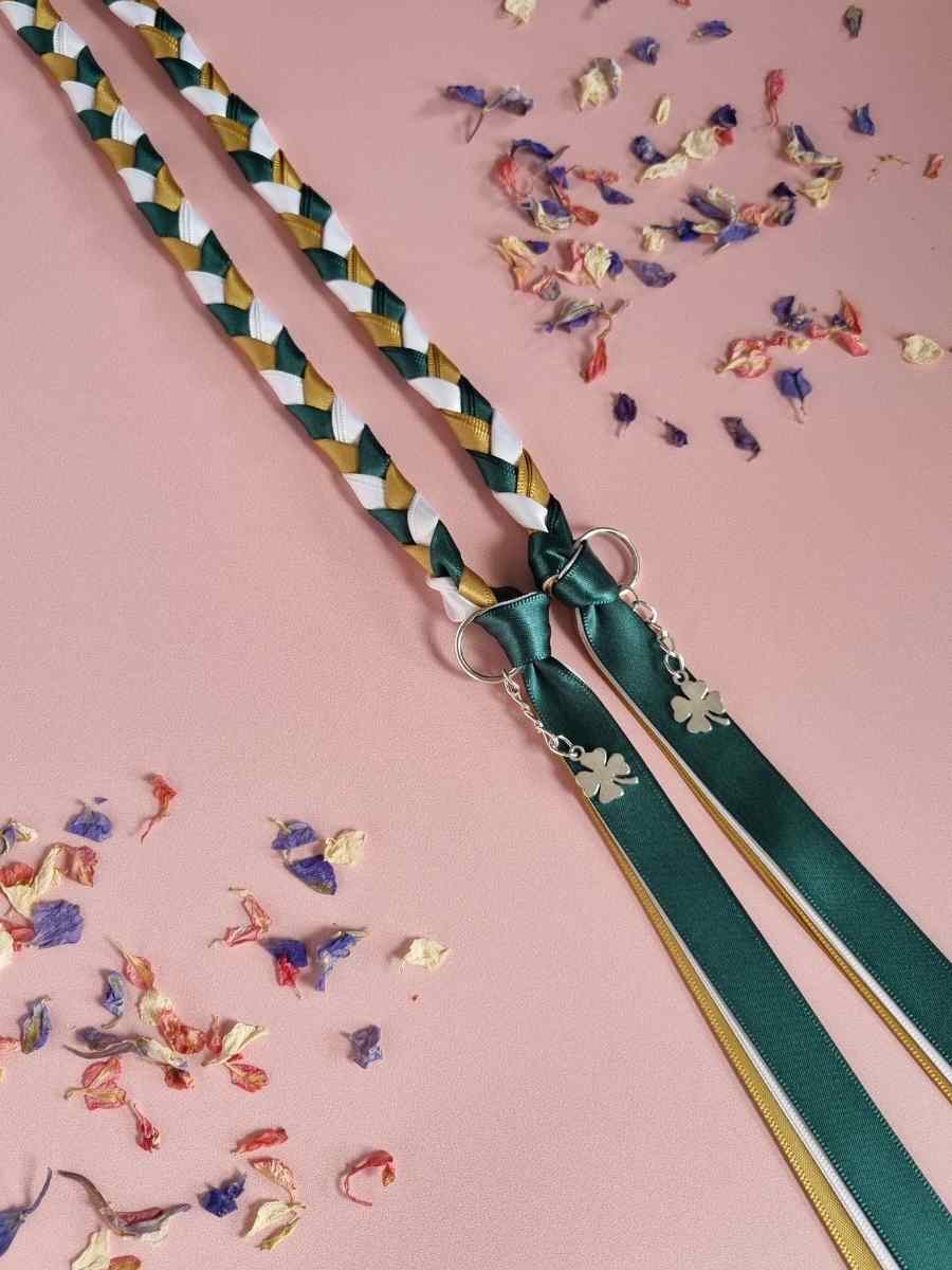 Intertwined Handfasting Cord made from green, white and gold strands of satin ribbon, along with silver shamrock charms.  Set against a pink backdrop with confetti.