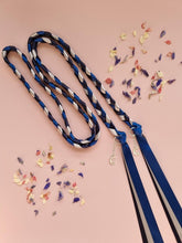 Load image into Gallery viewer, Intertwined Handfasting Cord made from silver, midnight blue and darkest blue coloured strands of satin ribbon, along with silver moon and star charms. Set against a pink backdrop with confetti.
