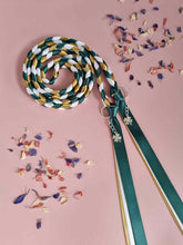 Load image into Gallery viewer, Intertwined Handfasting Cord made from green, ivory and gold satin ribbon, along with silver shamrock charms.  Set against a pink backdrop with confetti.
