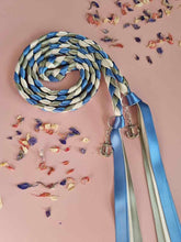 Load image into Gallery viewer, Intertwined Handfasting Cords made from blue, ivory and green strands of satin ribbon, along with silver anchor charms.  Set against a pink backdrop with confetti.
