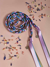 Load image into Gallery viewer, Intertwined Handfasting Cords made from mauve, blue and green strands of satin ribbon, along with silver celtic knot charms.  Set against a pink background with confetti.
