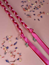 Load image into Gallery viewer, Intertwined Handfasting Cord made from pink, fuchsia and red strands of satin ribbon, along with silver rose charms.  Set against a pink background with confetti.
